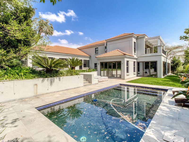 Rear view of a spacious two-story residence featuring a swimming pool, tiled patio area, and well-maintained garden with established landscaping.