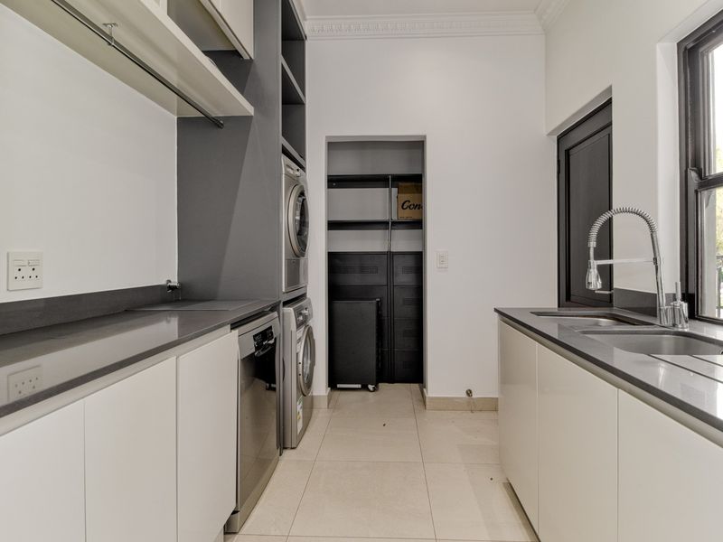 A modern, well-appointed scullery featuring sleek cabinetry, stone countertops, a double sink, and dedicated space for laundry appliances.