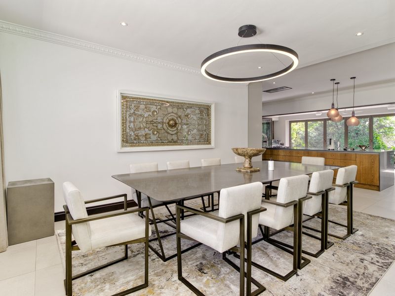 Spacious open-plan dining area featuring modern lighting, crown molding, and seamless flow into a contemporary kitchen with wood-toned cabinetry.