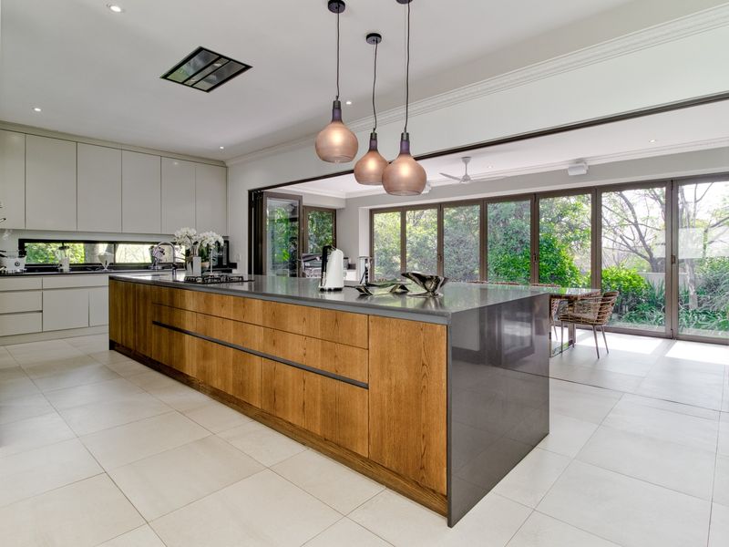 Modern open-plan kitchen featuring a large island with stone countertops, sleek cabinetry, and seamless indoor-outdoor flow through expansive bi-fold doors.