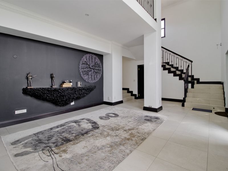 Spacious double-volume entrance hall featuring a modern staircase with wrought iron balustrade, tiled flooring, and a striking dark feature wall with built-in shelving.
