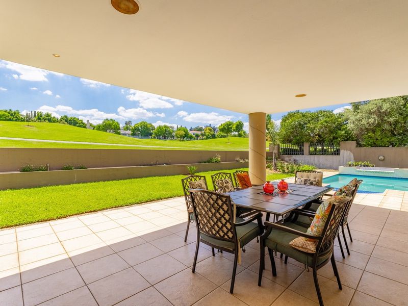 A spacious covered patio featuring tiled flooring and recessed lighting, overlooking a private swimming pool and landscaped garden with scenic views.
