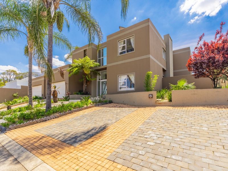 Modern double-story residential property featuring a paved driveway, double garage, and well-maintained landscaped garden with established palm trees.
