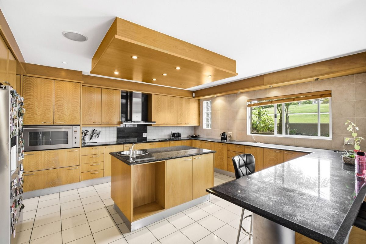 Spacious kitchen featuring light wood cabinetry, granite countertops, a central island, and integrated appliances with a modern drop ceiling design.
