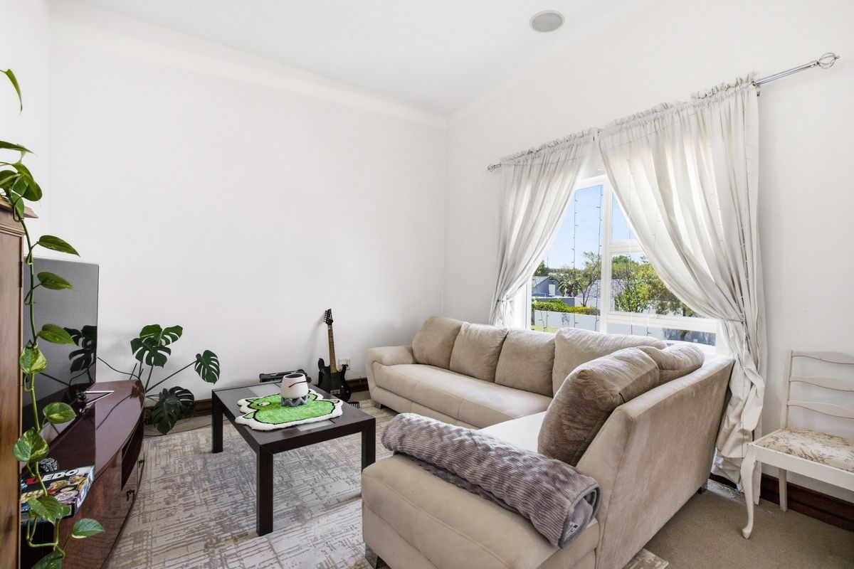 A bright and comfortable living room featuring neutral walls, carpeted flooring, and a large window that allows for ample natural light.