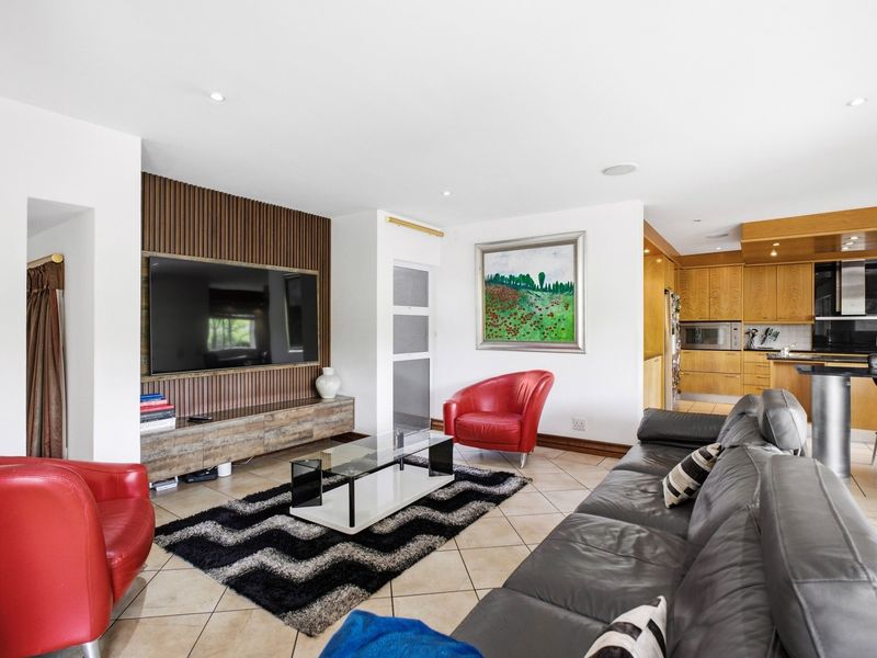 Spacious open-plan living area featuring a modern slatted timber feature wall, tiled flooring, and a well-appointed kitchen with integrated appliances and breakfast bar.