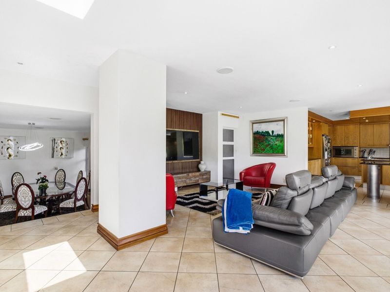 Spacious open-plan living area featuring tiled floors, recessed lighting, and a well-appointed kitchen with integrated appliances and timber cabinetry.