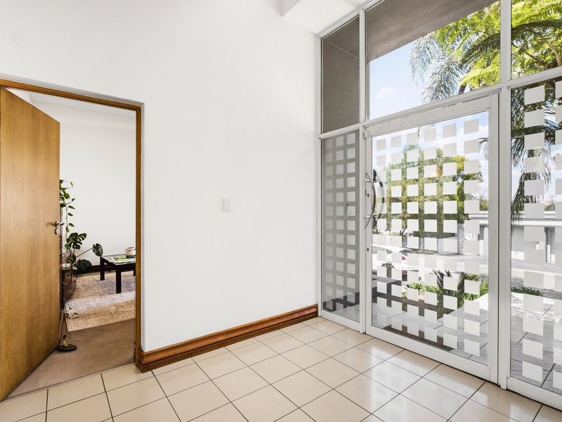 Bright entrance foyer featuring tiled flooring, timber door frame, and large glass panels providing natural light and a view to the exterior.