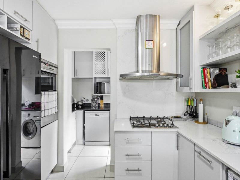 Modern kitchen featuring stone countertops, gas hob, stainless steel extractor fan, and built-in cabinetry, with an adjacent scullery area.
