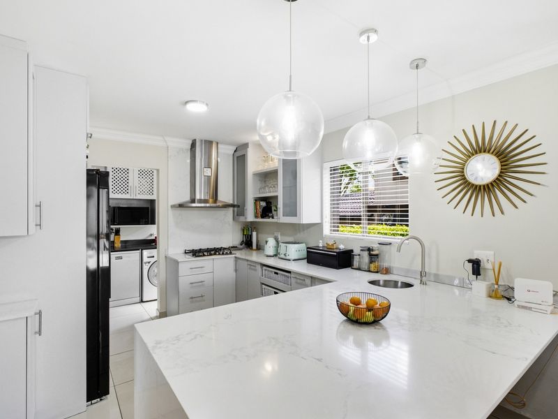 Modern kitchen featuring white quartz countertops, gas hob, stainless steel extractor, and a functional scullery area with clean, contemporary finishes.