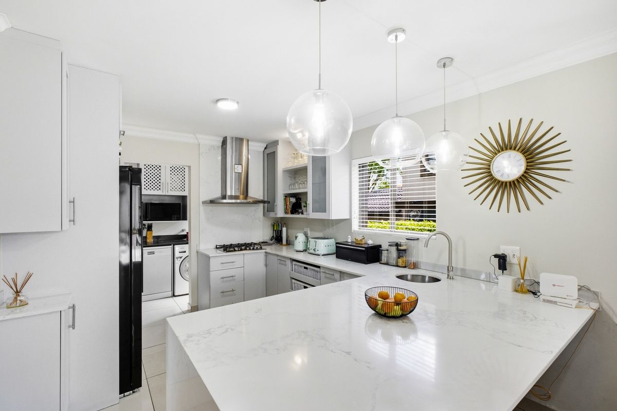 Modern kitchen featuring white quartz countertops, gas hob, stainless steel extractor, and a functional scullery area with clean, contemporary finishes.