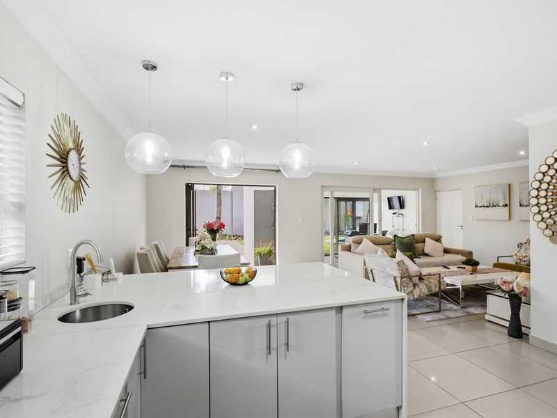 Modern open-plan living area featuring a sleek kitchen island with stone countertops, pendant lighting, and seamless flow to the outdoor patio through sliding glass doors.