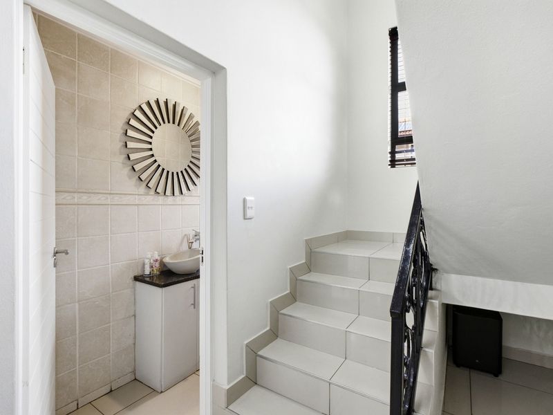A bright hallway featuring a tiled staircase with a wrought iron balustrade, leading to a small guest bathroom with a vanity and vessel sink.