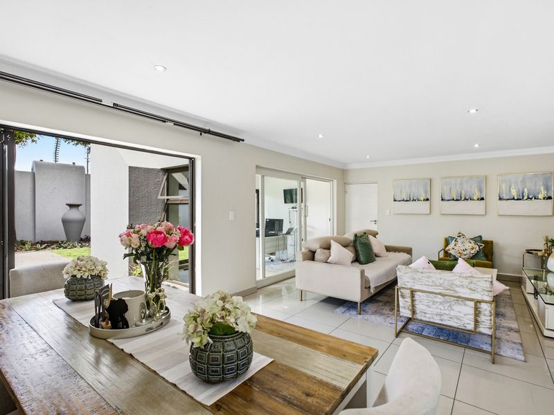 Spacious open-plan living and dining area featuring neutral tiled flooring, recessed lighting, and seamless indoor-outdoor flow through large sliding and bi-fold glass doors.