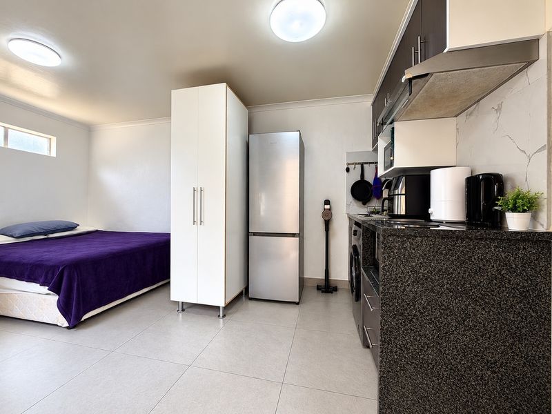 Compact open-plan studio apartment featuring a functional kitchenette with stone countertops, built-in cabinetry, and tiled flooring throughout.