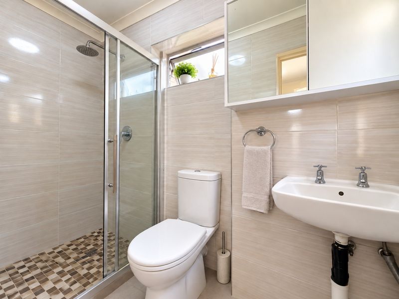 A well-maintained bathroom featuring a glass-enclosed shower, mosaic floor tiling, wall-mounted vanity cabinet, and neutral ceramic wall finishes.