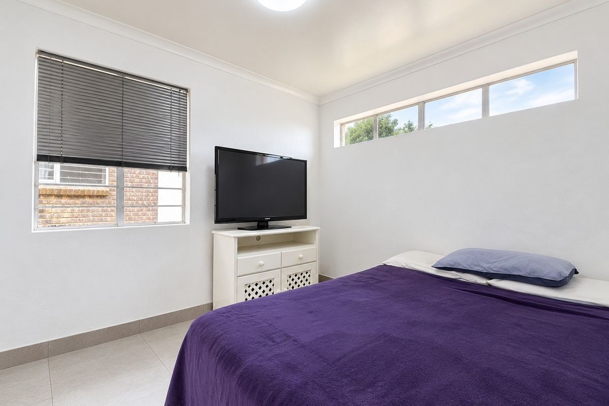 A functional bedroom featuring tiled flooring, a clerestory window for natural light, and venetian blinds.