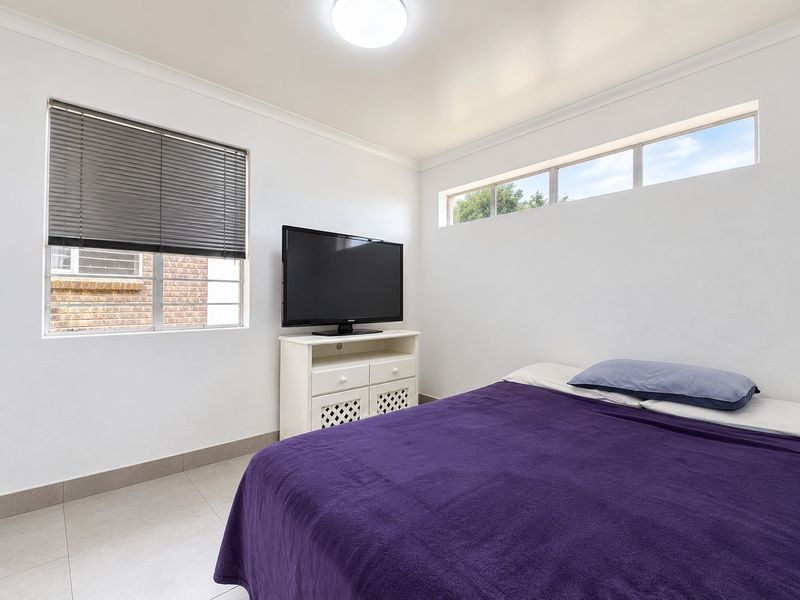A functional bedroom featuring tiled flooring, a clerestory window for natural light, and venetian blinds.