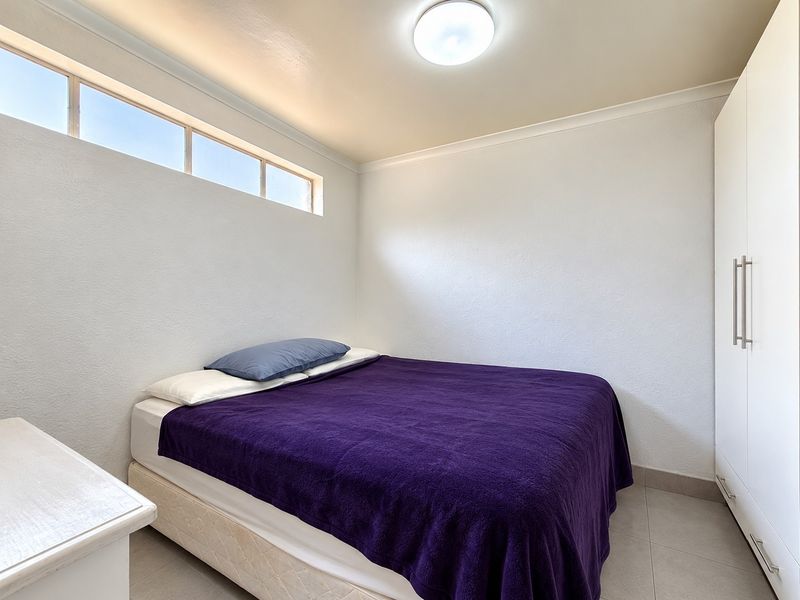 A clean bedroom featuring tiled flooring, a built-in wardrobe, and a high-level clerestory window providing natural light.