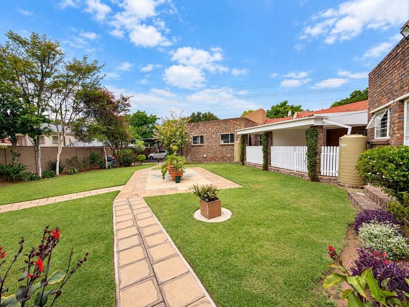 A well-maintained rear garden featuring a paved walkway, lush lawn, covered patio area, and brick exterior facade with a water tank.
