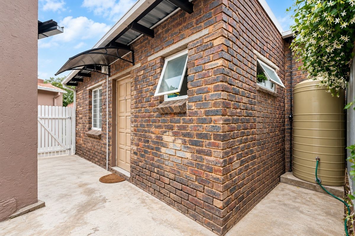 Rear exterior view of the property featuring face brick walls, a water storage tank, concrete paving, and a small entrance awning.