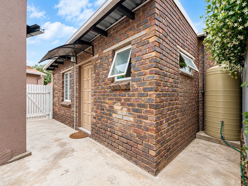 Rear exterior view of the property featuring face brick walls, a water storage tank, concrete paving, and a small entrance awning.