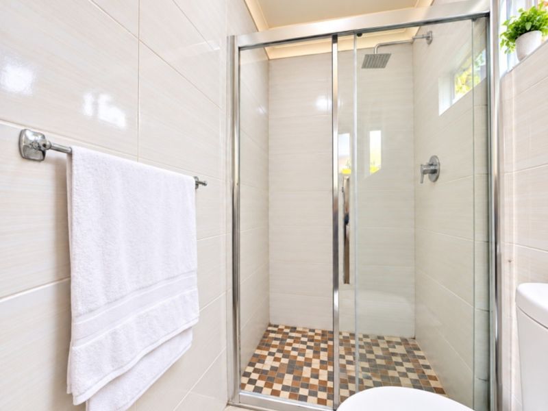 A clean, modern bathroom featuring a walk-in shower with a glass enclosure, mosaic floor tiling, and neutral wall tiles.