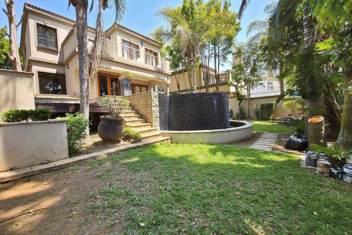Rear exterior view of a multi-story cluster home featuring a raised wooden deck, stone staircase, and a decorative tiled water feature in the garden.