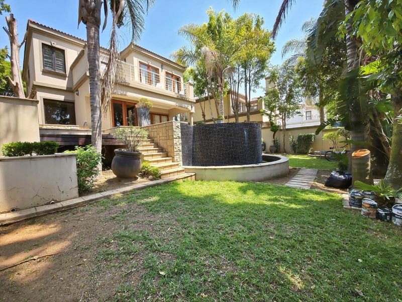 Rear exterior view of a multi-story cluster home featuring a raised wooden deck, stone staircase, and a decorative tiled water feature in the garden.