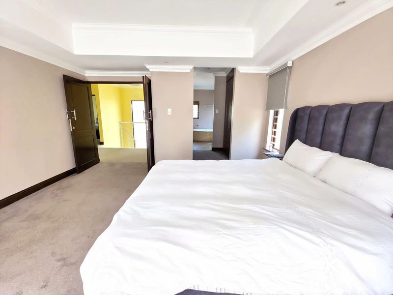 Spacious bedroom featuring a tray ceiling with recessed lighting, neutral wall tones, plush carpeting, and direct access to an en-suite bathroom area.