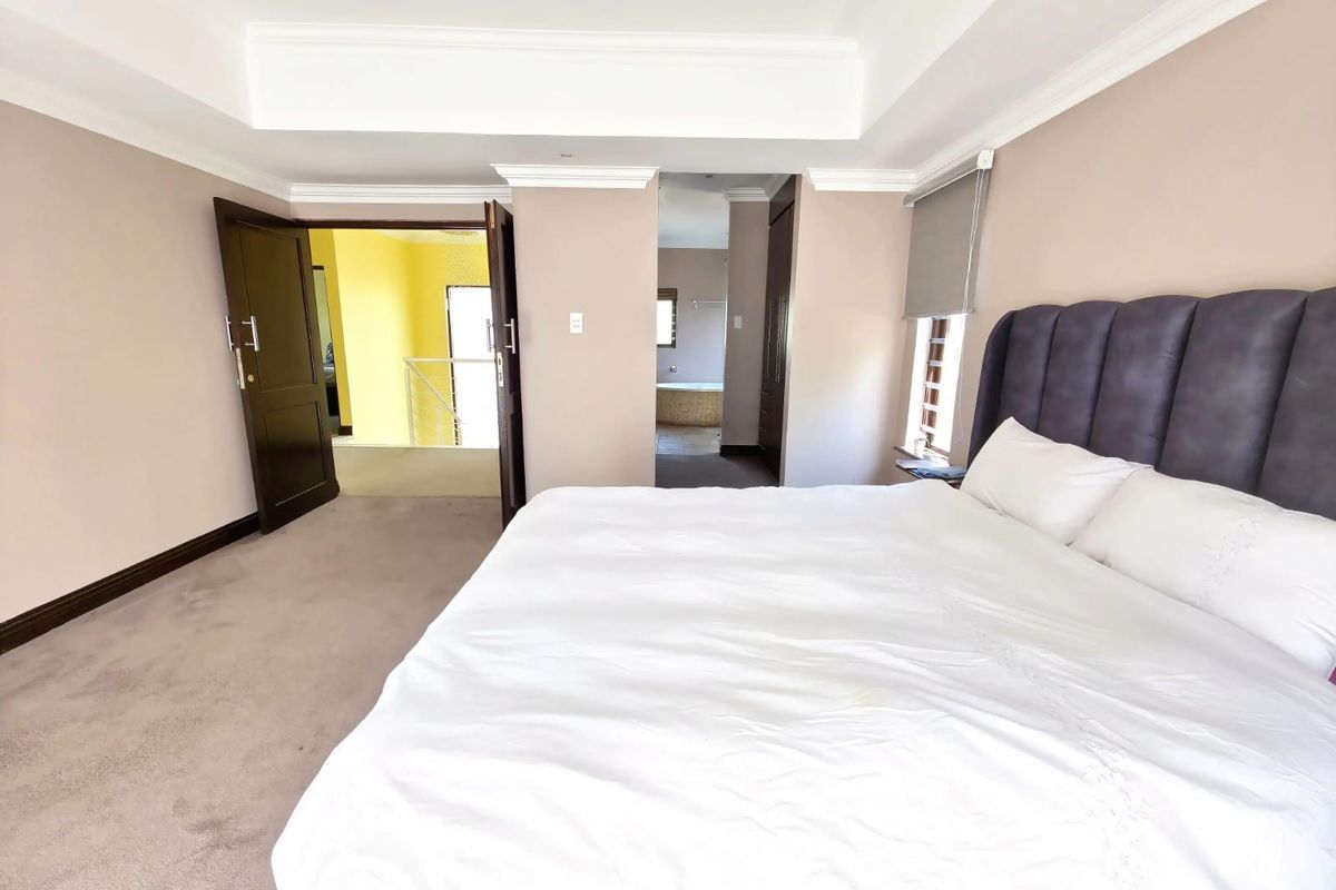 Spacious bedroom featuring a tray ceiling with recessed lighting, neutral wall tones, plush carpeting, and direct access to an en-suite bathroom area.