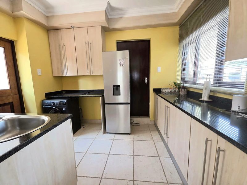 A functional kitchen featuring granite countertops, light wood-finish cabinetry, tiled flooring, and a coved ceiling, offering a practical layout for daily meal preparation.