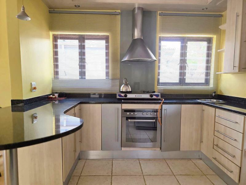 A functional kitchen featuring light wood cabinetry, dark granite countertops, a breakfast bar, and built-in stainless steel appliances including an oven and gas hob.