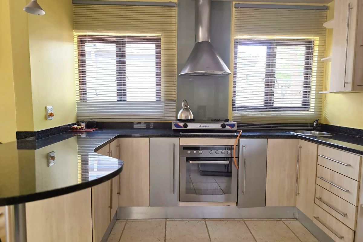 A functional kitchen featuring light wood cabinetry, dark granite countertops, a breakfast bar, and built-in stainless steel appliances including an oven and gas hob.
