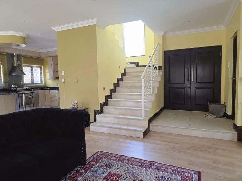 Open plan living area featuring a tiled staircase with metal balustrade, double entrance doors, and a modern kitchen with built-in appliances.
