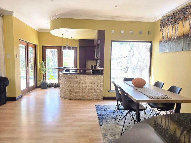 Spacious open-plan living and dining area featuring a built-in bar with stone cladding, laminate flooring, and large windows providing natural light and garden access.