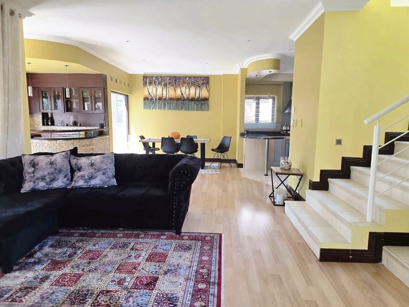 Spacious open-plan living and dining area featuring laminate flooring, a staircase, and a functional kitchen with granite countertops and ample cabinetry.