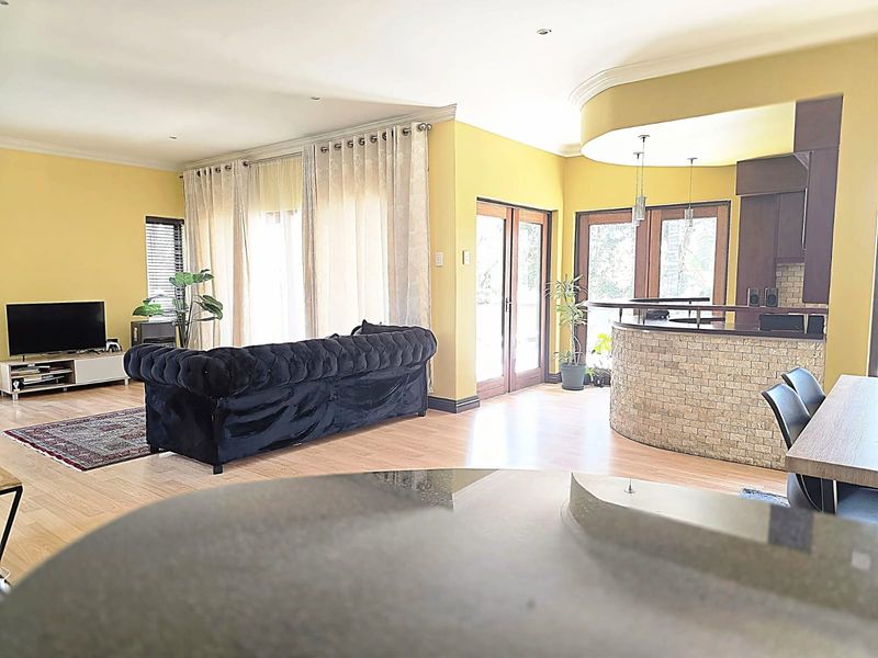 Spacious open-plan living area featuring a built-in bar with stone cladding, laminate flooring, and direct access to the outdoors through double glass doors.