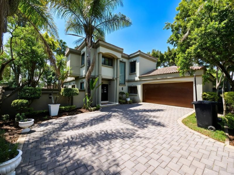 A well-maintained double-story cluster home featuring a paved driveway, double garage, and established garden surroundings.
