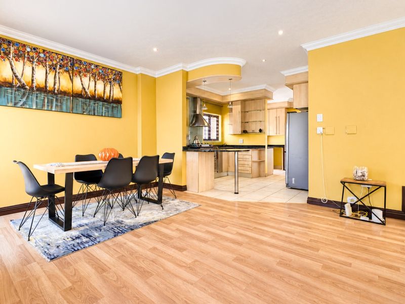 Open-plan living and dining area featuring laminate flooring, crown molding, and a functional kitchen with built-in cabinetry and granite countertops.