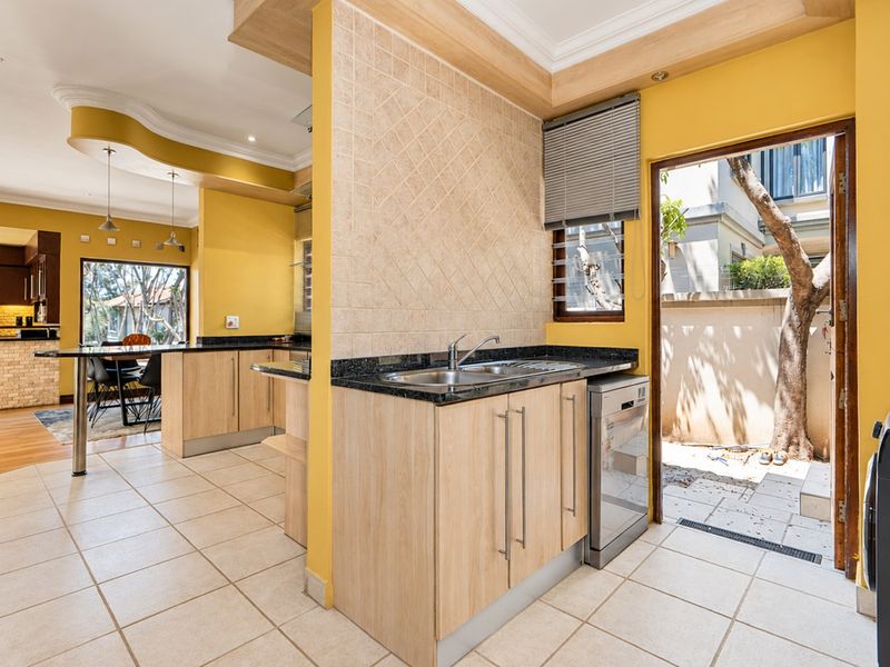 Functional scullery area featuring granite countertops, light wood cabinetry, and direct access to an outdoor courtyard, seamlessly connected to the main kitchen space.