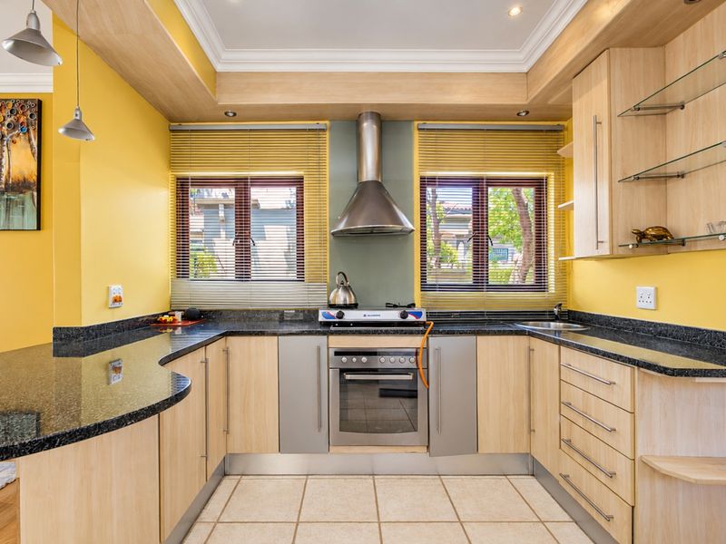 A well-maintained kitchen featuring granite countertops, light wood cabinetry, built-in oven with gas hob, and stainless steel extractor fan.