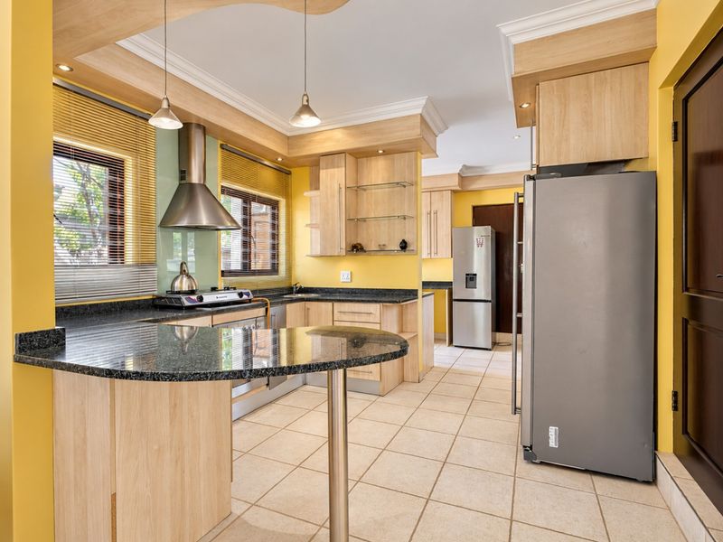 A well-maintained kitchen featuring light wood cabinetry, granite countertops, a breakfast bar, and modern stainless steel fixtures with tiled flooring.