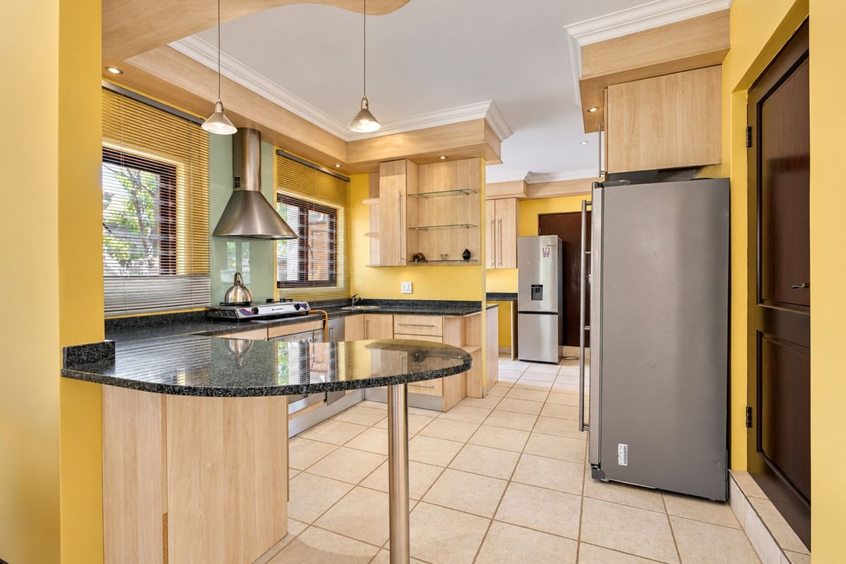 A well-maintained kitchen featuring light wood cabinetry, granite countertops, a breakfast bar, and modern stainless steel fixtures with tiled flooring.