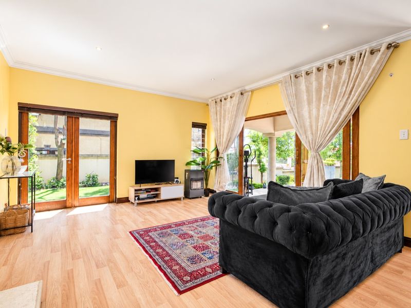 Spacious living room featuring light laminate flooring, crown molding, and large wooden-framed glass doors providing direct access to the garden and patio area.