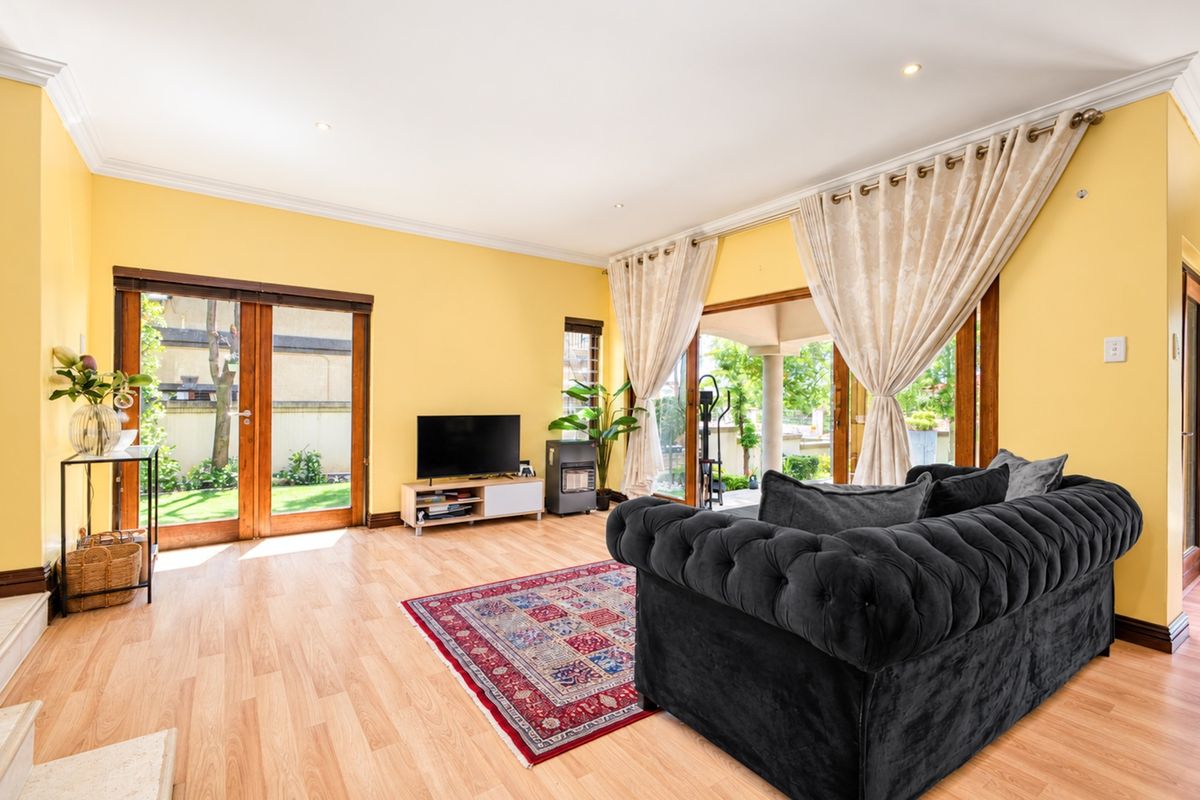 Spacious living room featuring light laminate flooring, crown molding, and large wooden-framed glass doors providing direct access to the garden and patio area.
