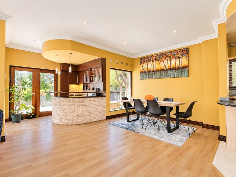 Spacious open-plan dining and bar area featuring laminate flooring, a custom stone-clad built-in bar, and direct access to the outdoor patio through glass doors.