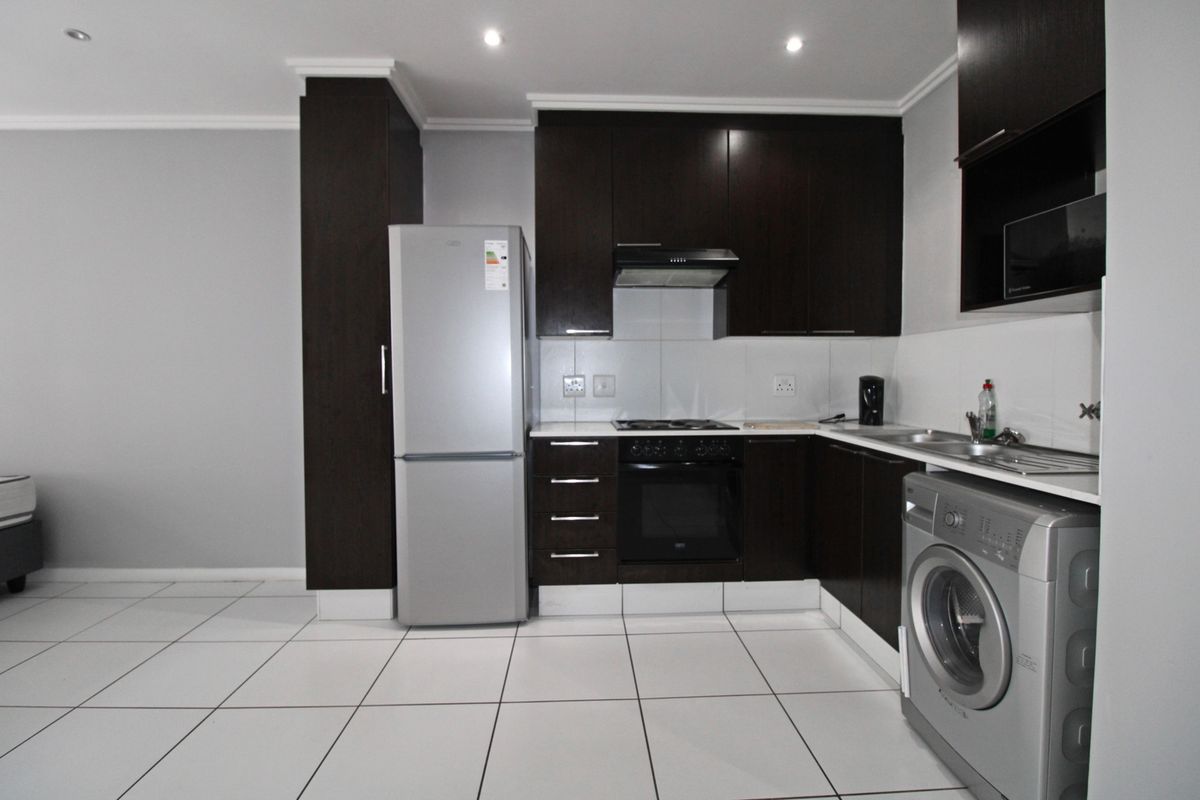 A functional kitchen featuring dark wood cabinetry, built-in oven, hob, extractor fan, and tiled flooring, providing a clean and practical cooking space.