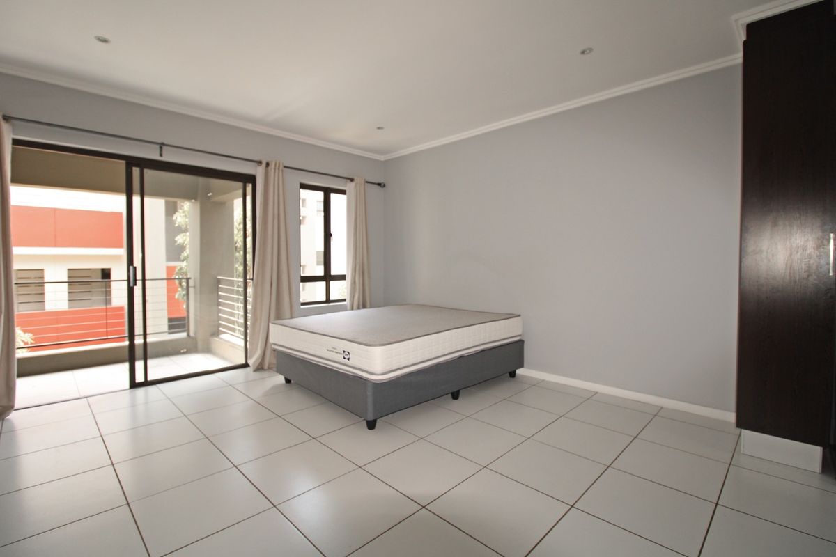 Spacious bedroom featuring neutral tiled flooring, built-in cupboards, recessed lighting, and a sliding glass door providing access to a private balcony.