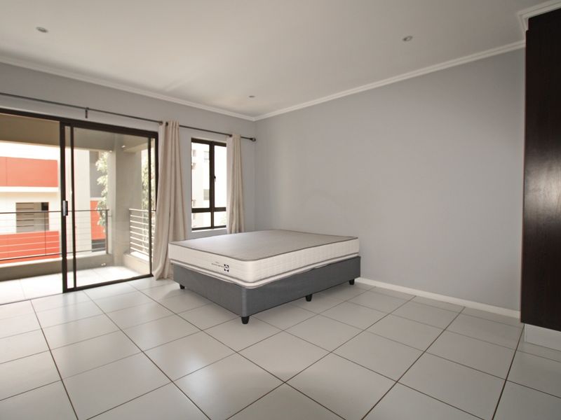 Spacious bedroom featuring neutral tiled flooring, built-in cupboards, recessed lighting, and a sliding glass door providing access to a private balcony.